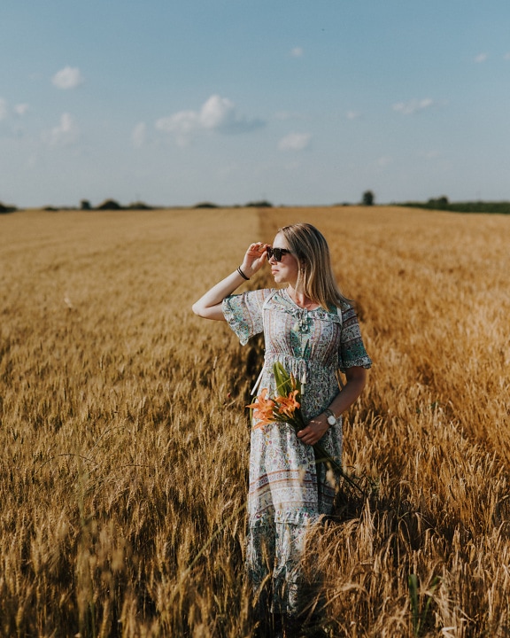 Người phụ nữ trẻ nông thôn tuyệt đẹp đi bộ trên cánh đồng lúa mì vào mùa hè