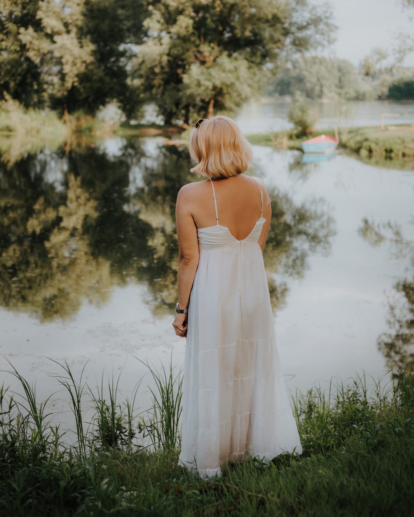 Femeie într-o rochie albă fără spate stând lângă apă