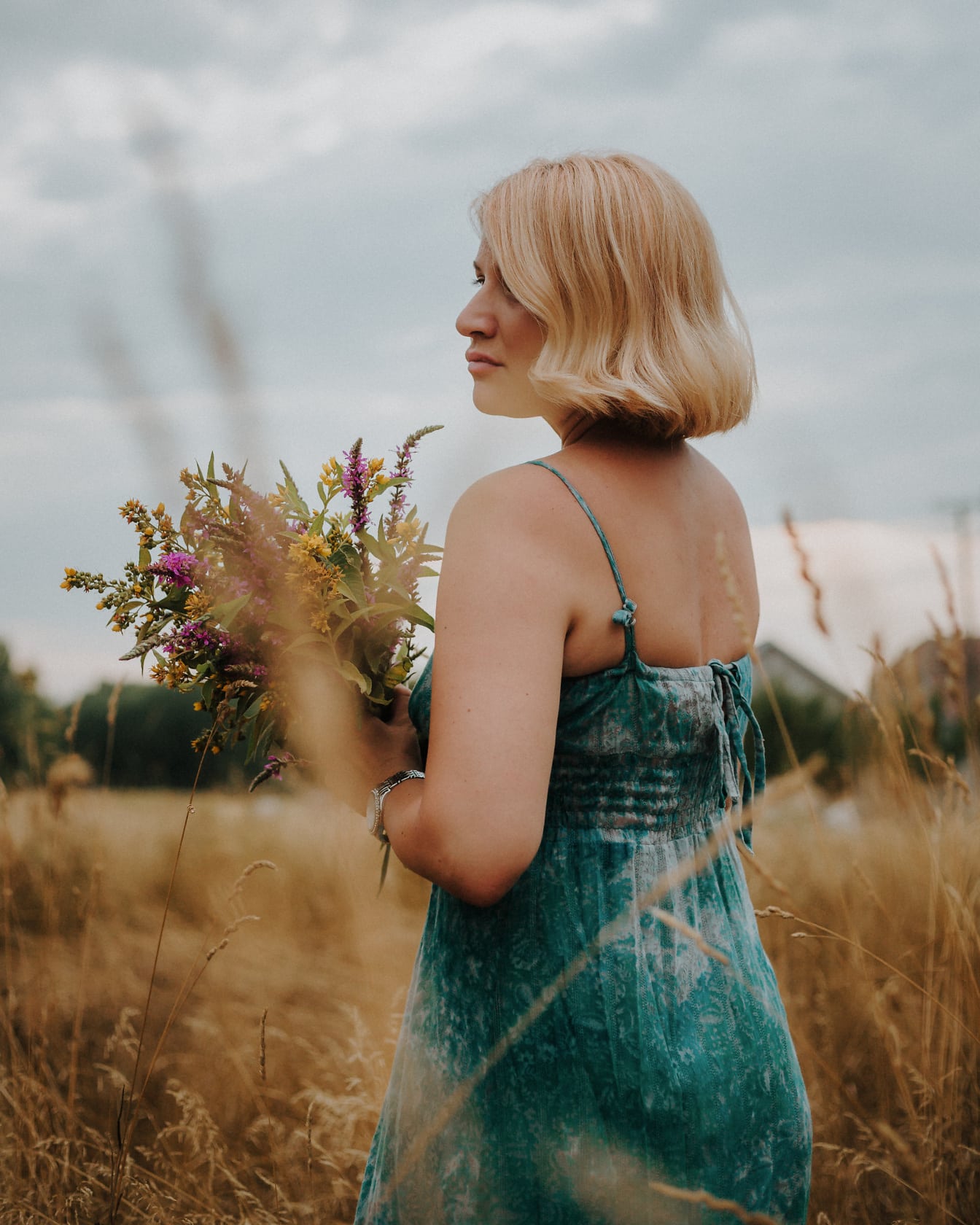 Donna bionda che tiene mazzo di fiori in un campo estivo asciutto