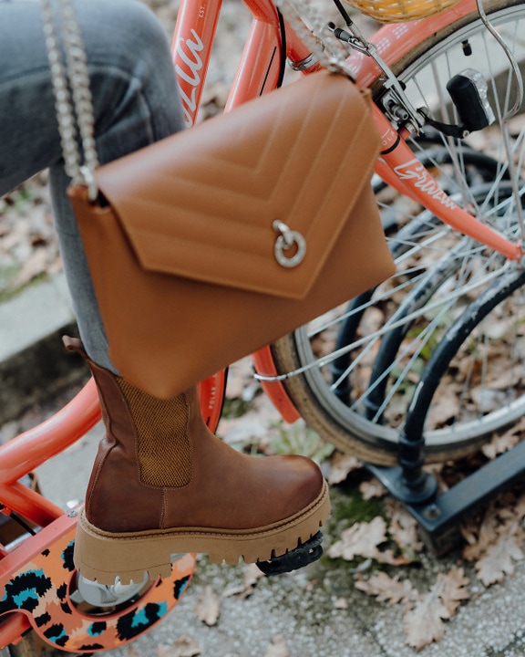 Person wearing a fashionable brown leather boot and a brown purse on a red bicycle