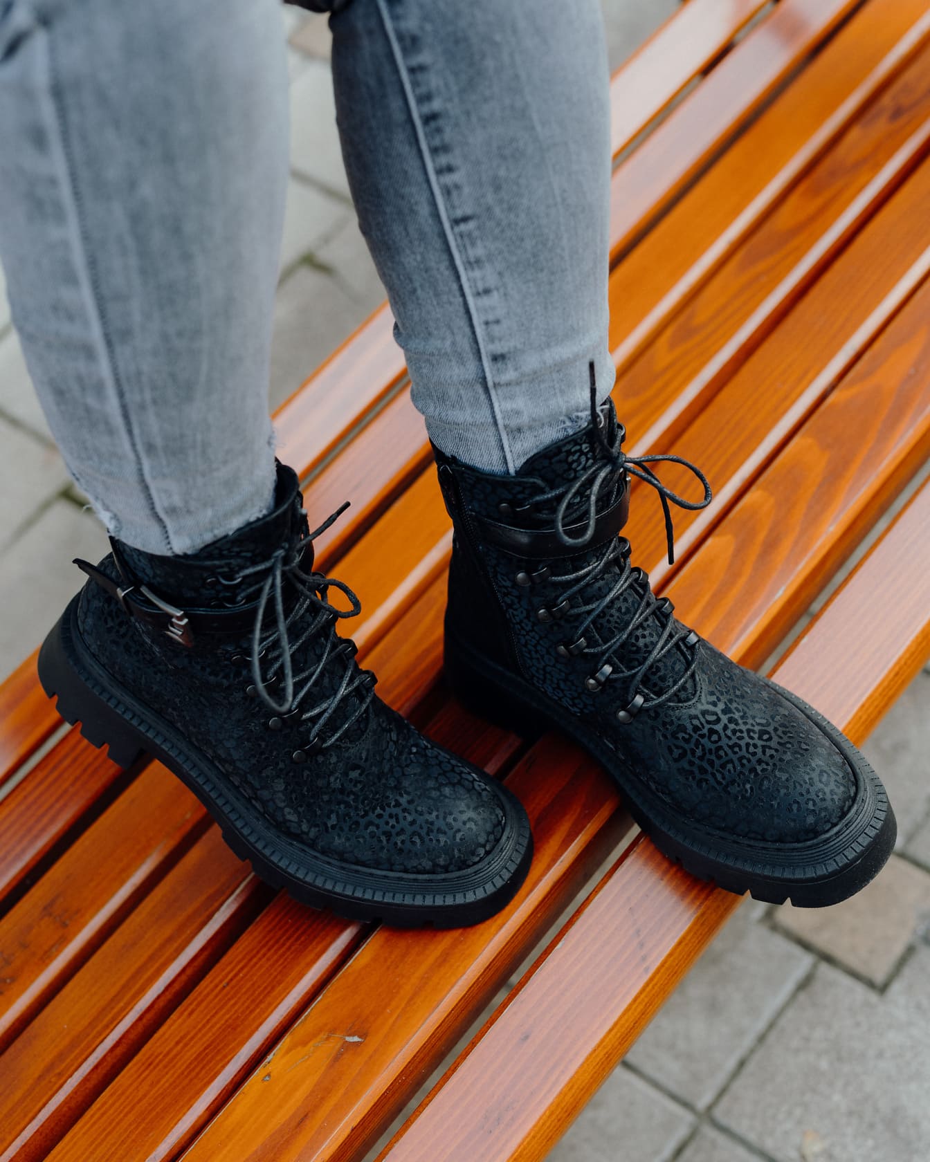 Nohy osoby v módních černých botách na dřevěné lavici