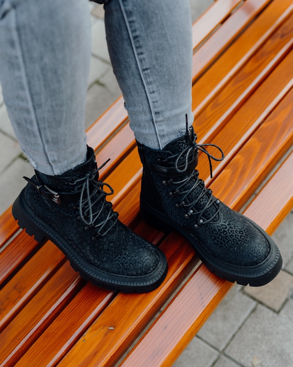 Person’s legs wearing fashionable black boots on wooden bench