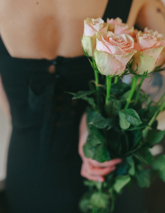 Mujer sosteniendo un ramo de rosas rosas brillantes en su espalda