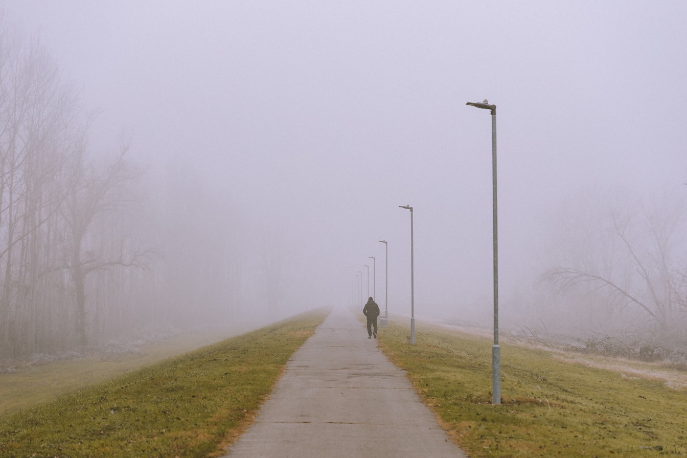 Orang berjalan di jalan aspal pada hari berkabut