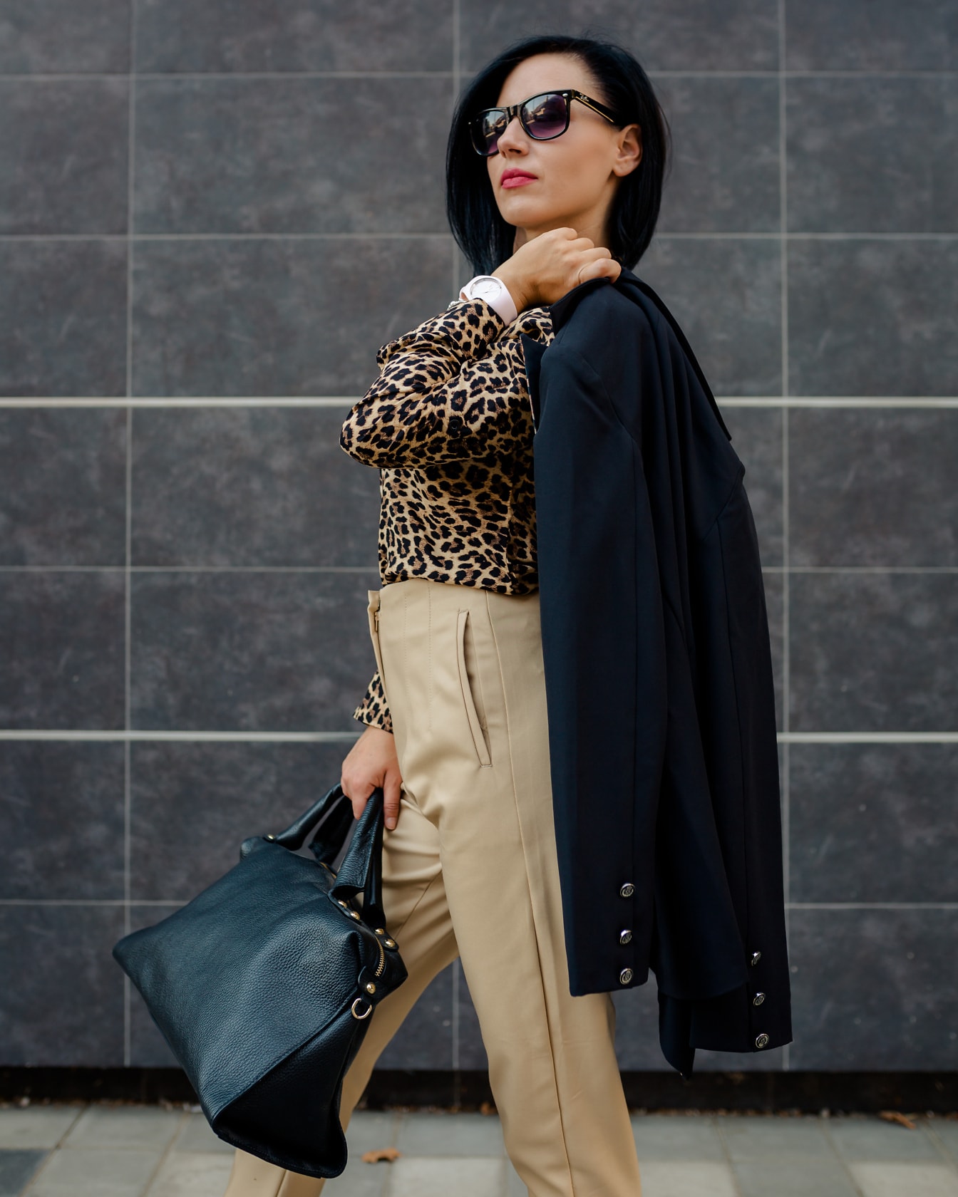Affärskvinna i leopardmönstrad skjorta och fashionabla byxor som rymmer en svart väska