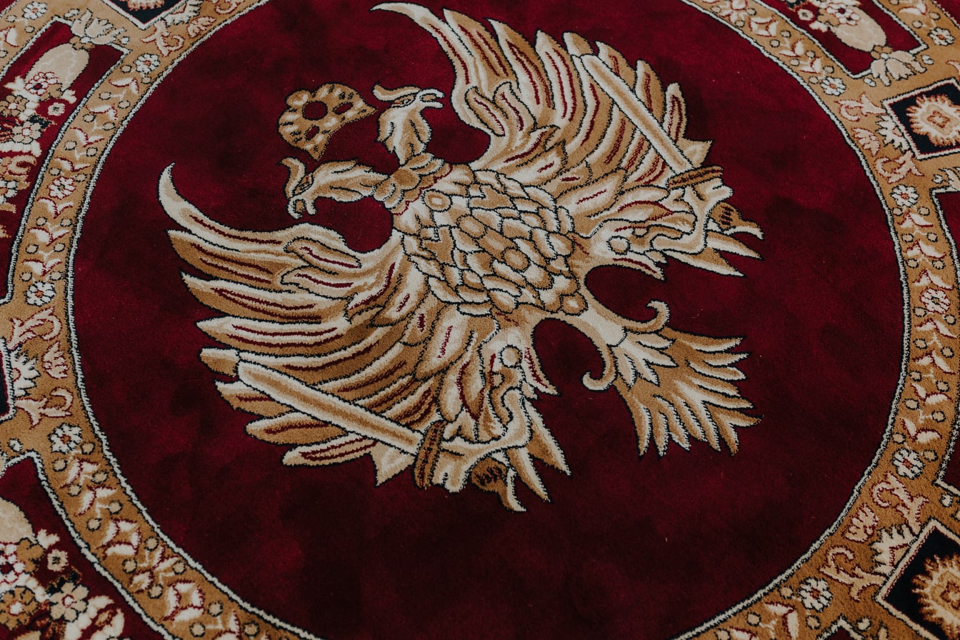 赤と金の典礼用絨毯に2頭の鷲のイラストが描かれている