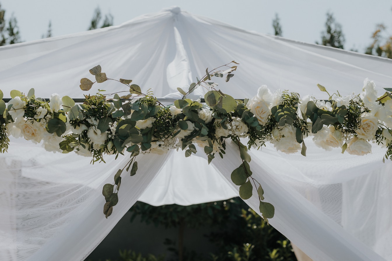 Dosel blanco con flores blancas y hojas verdes en el lugar de la boda