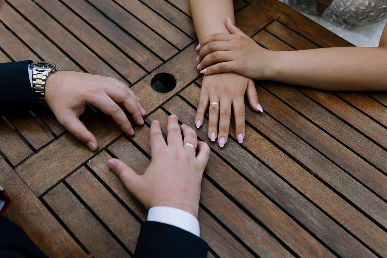 나무 테이블에 결혼 반지를 끼고 있는 한 쌍의 손