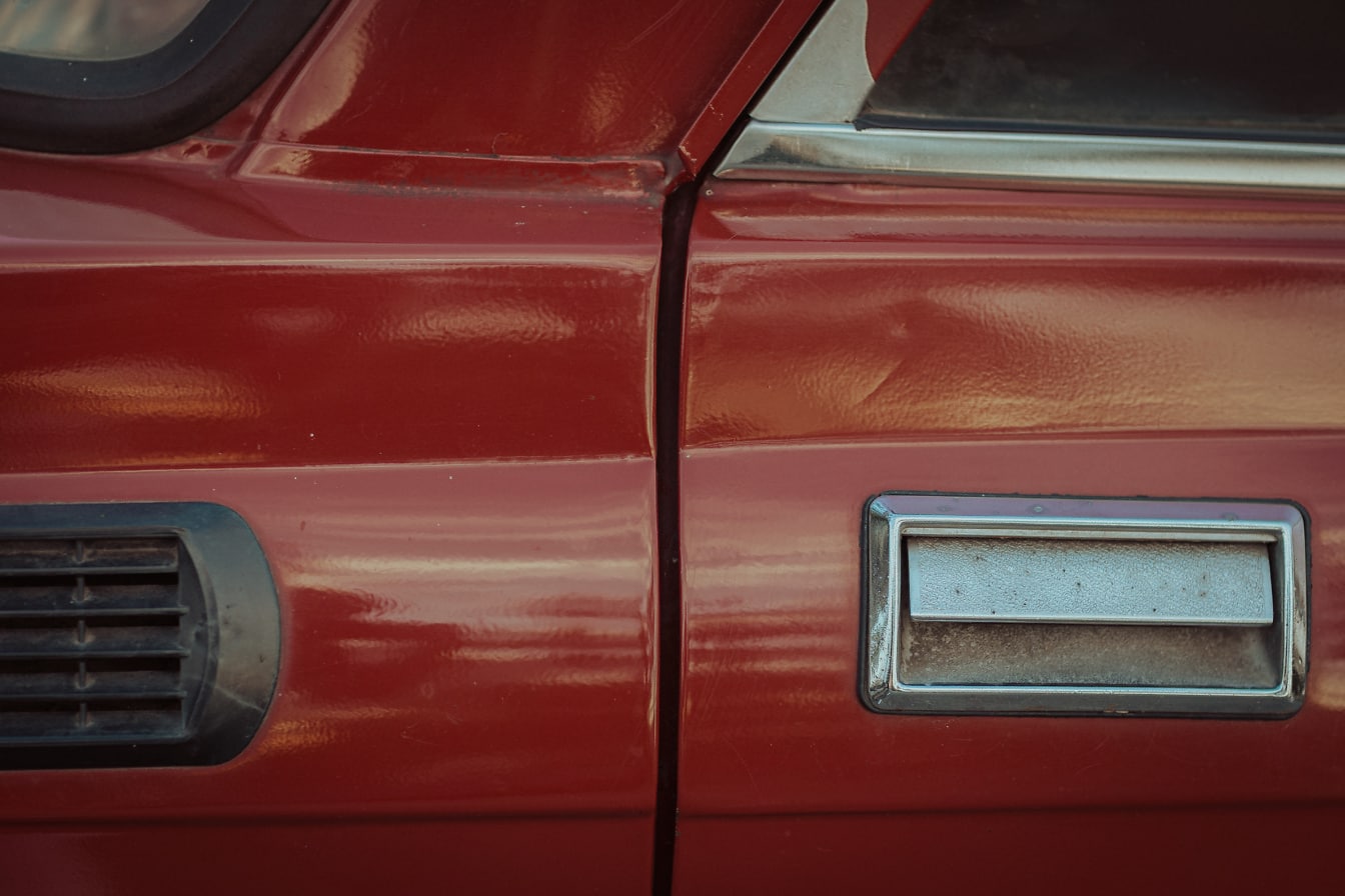 Kovová kľučka dverí na tmavočervenom starom aute