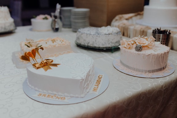 Meja dengan kue pengantin putih dengan hiasan pita emas di atasnya
