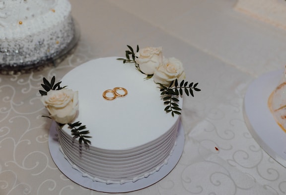 White wedding cake with gold wedding rings on top and white roses as decoration