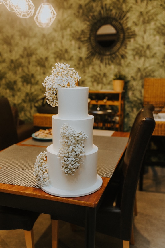 Eine dreistöckige weiße Hochzeitstorte mit Blumen auf dem Tisch im Restaurant