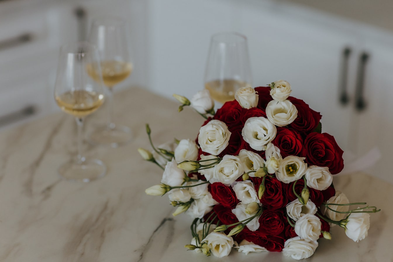 Букет от червени и бели рози на мраморна маса с чаши бяло вино на заден план