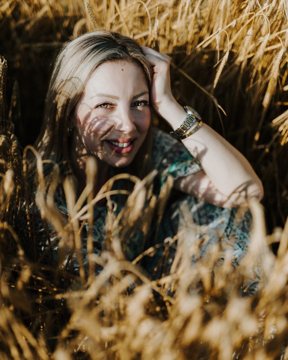Pekne vyzerajúca žena sedí na pšeničnom poli a usmieva sa