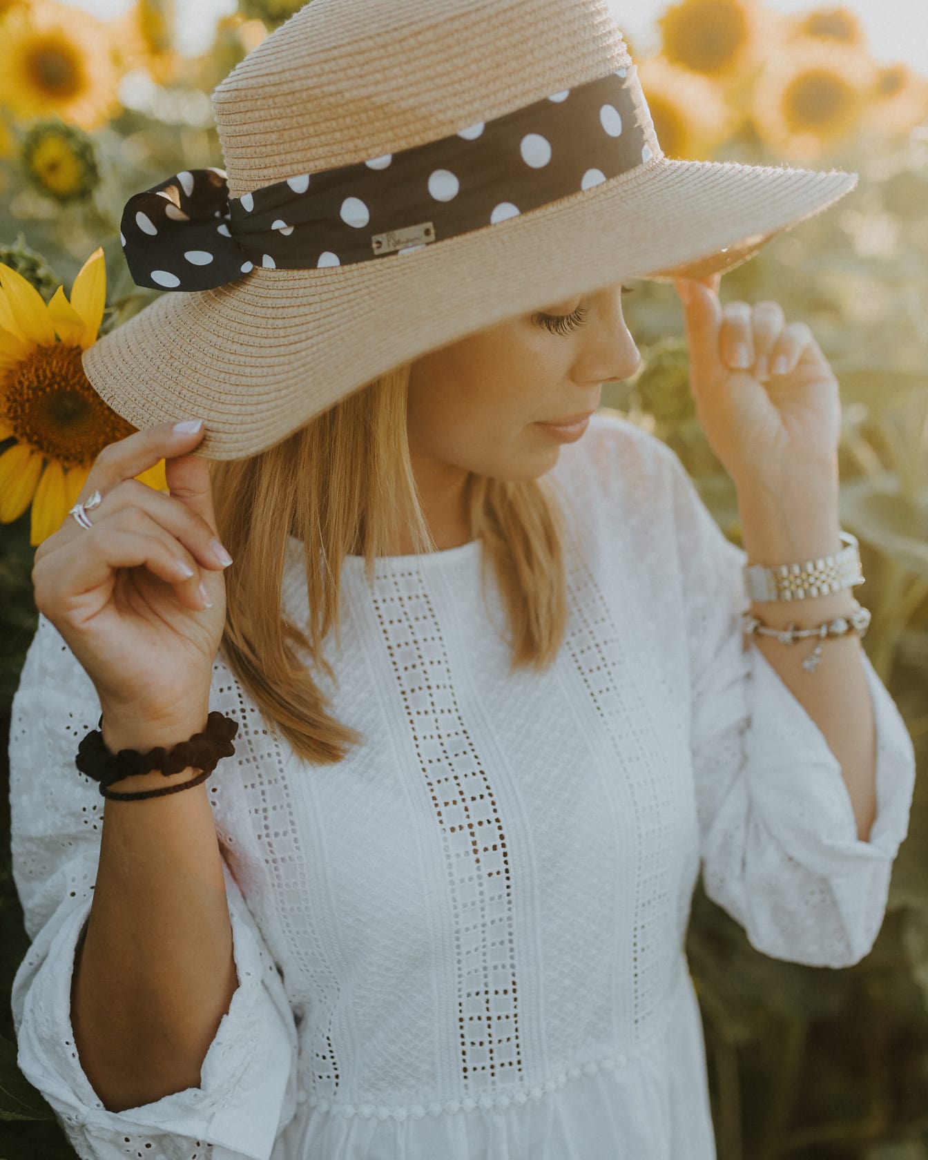 Жена, носеща шапка и гледаща надолу към слънчогледово поле със слънчева светлина на заден план