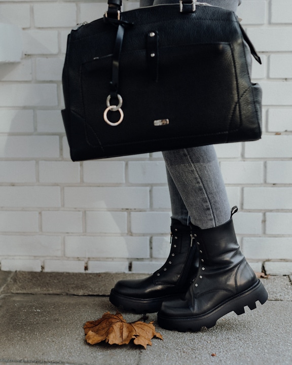 Jambes d’une personne avec des bottes noires modernes et un sac en cuir noir