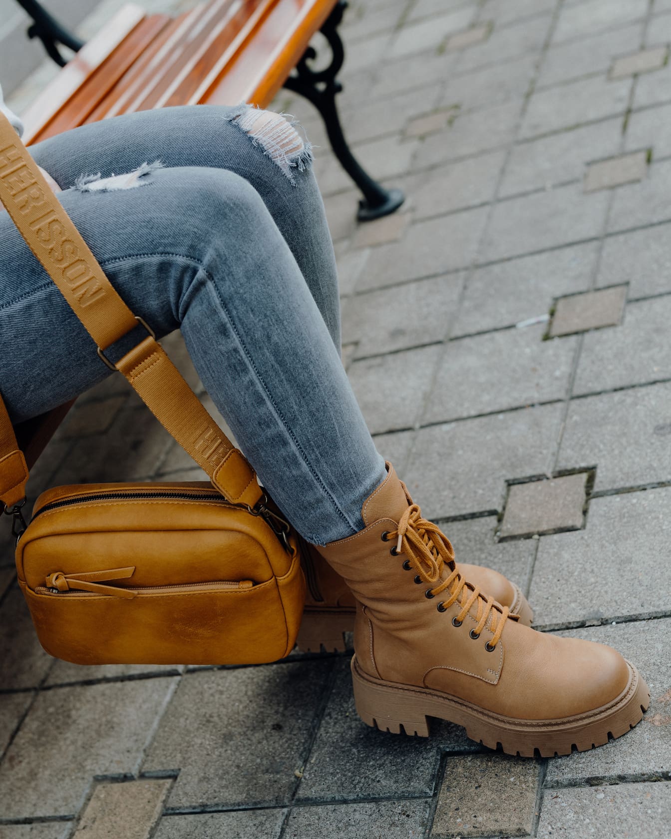 坐在长凳上的人穿着现代破洞牛仔裤，穿着淡黄色的钱包和靴子