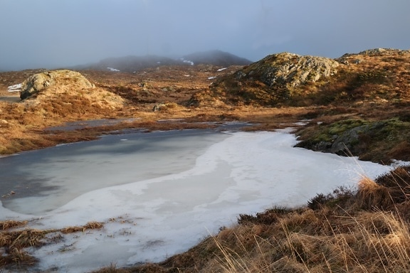 Frozen lake in a valley with foggy hills in backgrounds
