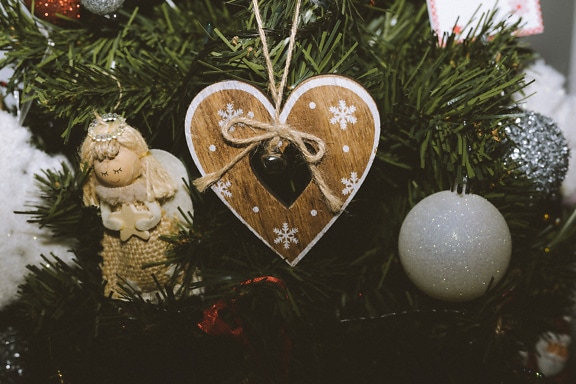 Ornamento de madeira em forma de coração e estatueta de anjo feita à mão em uma árvore de Natal
