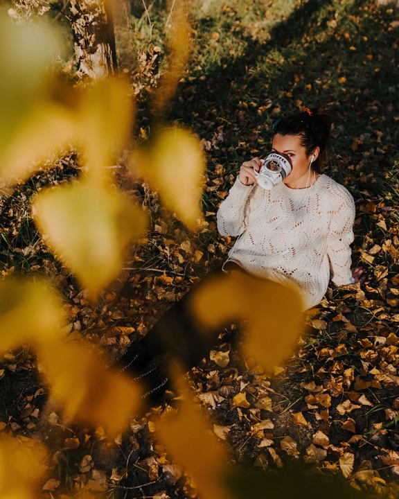Woman in handmade wool sweater sitting on the ground and drinking from big coffee mug