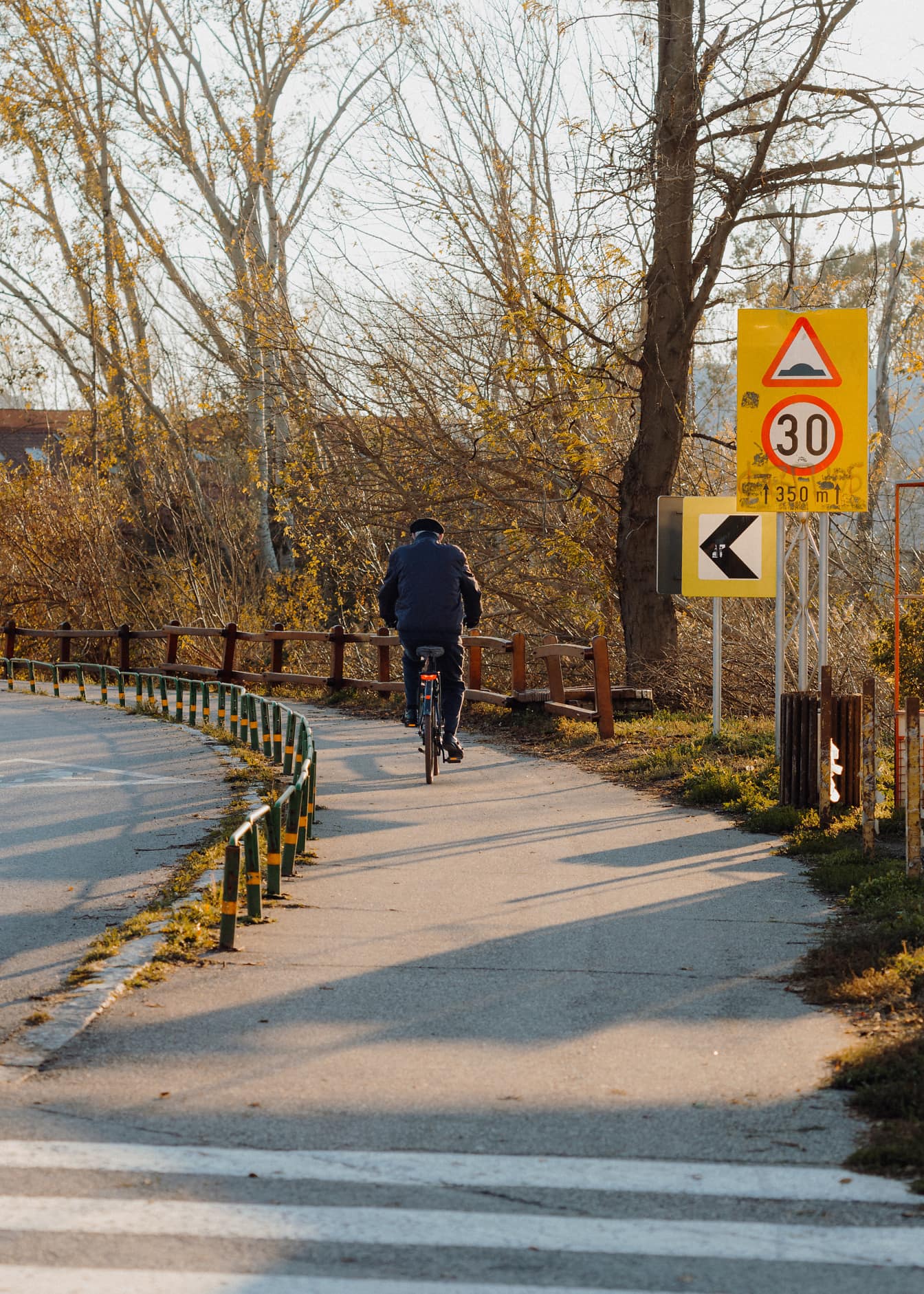 Vieil homme faisant du vélo sur une piste goudronnée avec panneau de signalisation sur la route à 30 km/h