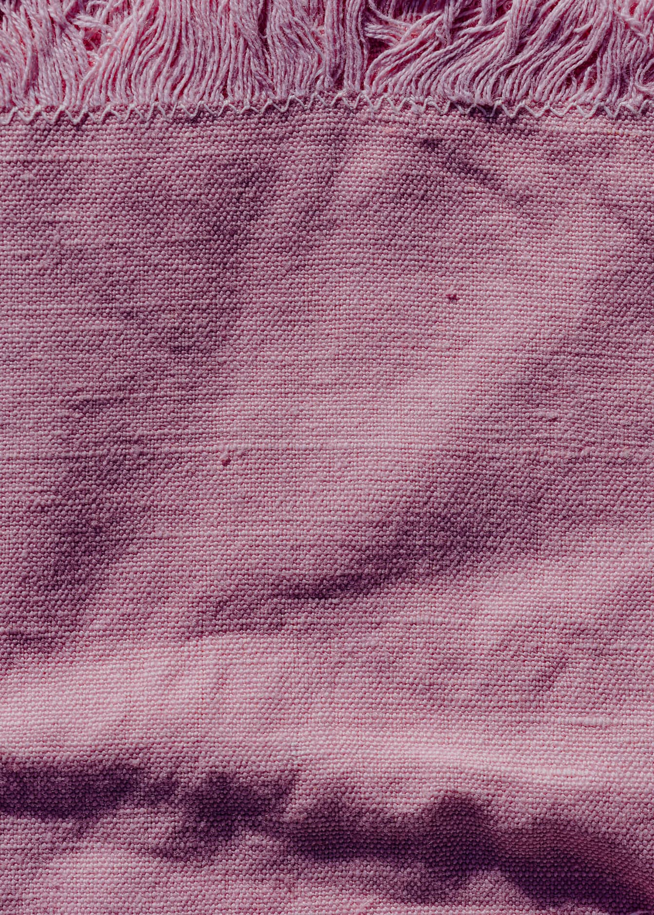 Textur eines rauen Leinenstoffs rosafarben mit Fransen am Rand