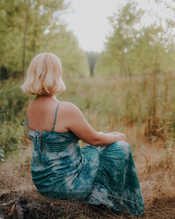 Back-turned woman in satin backless dress sitting in a field