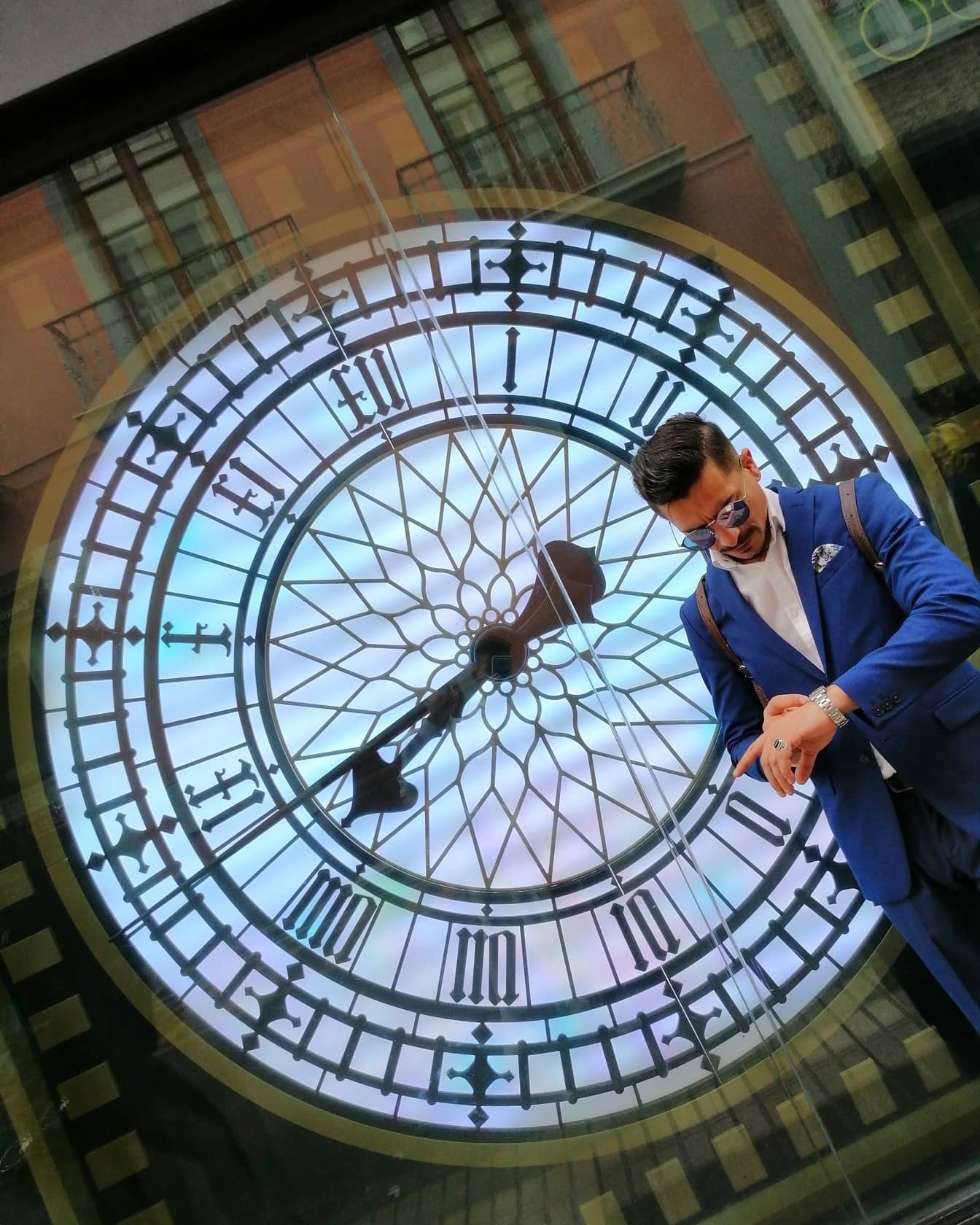 양복을 입은 사업가가 배경에 있는 창문에 큰 시계가 반사되어 손목시계를 보고 있다