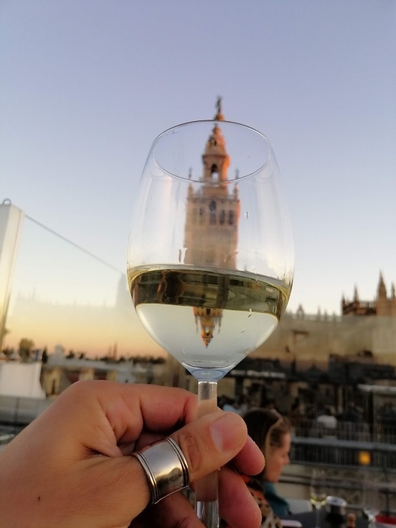 Hånden holder et glas hvidvin med en refleksion af tårnet i baggrunden