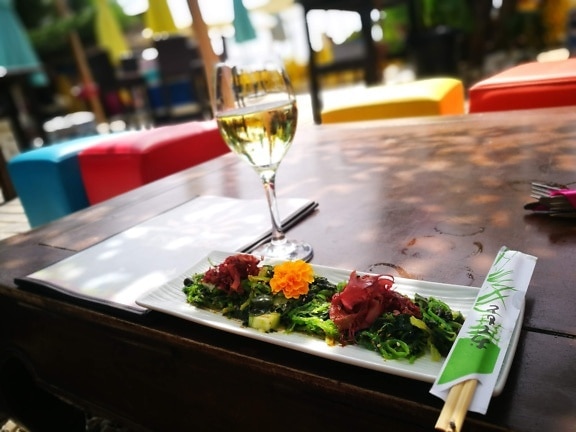 木の棒と白ワインのグラスを並べたテーブルの上に海藻料理のプレート