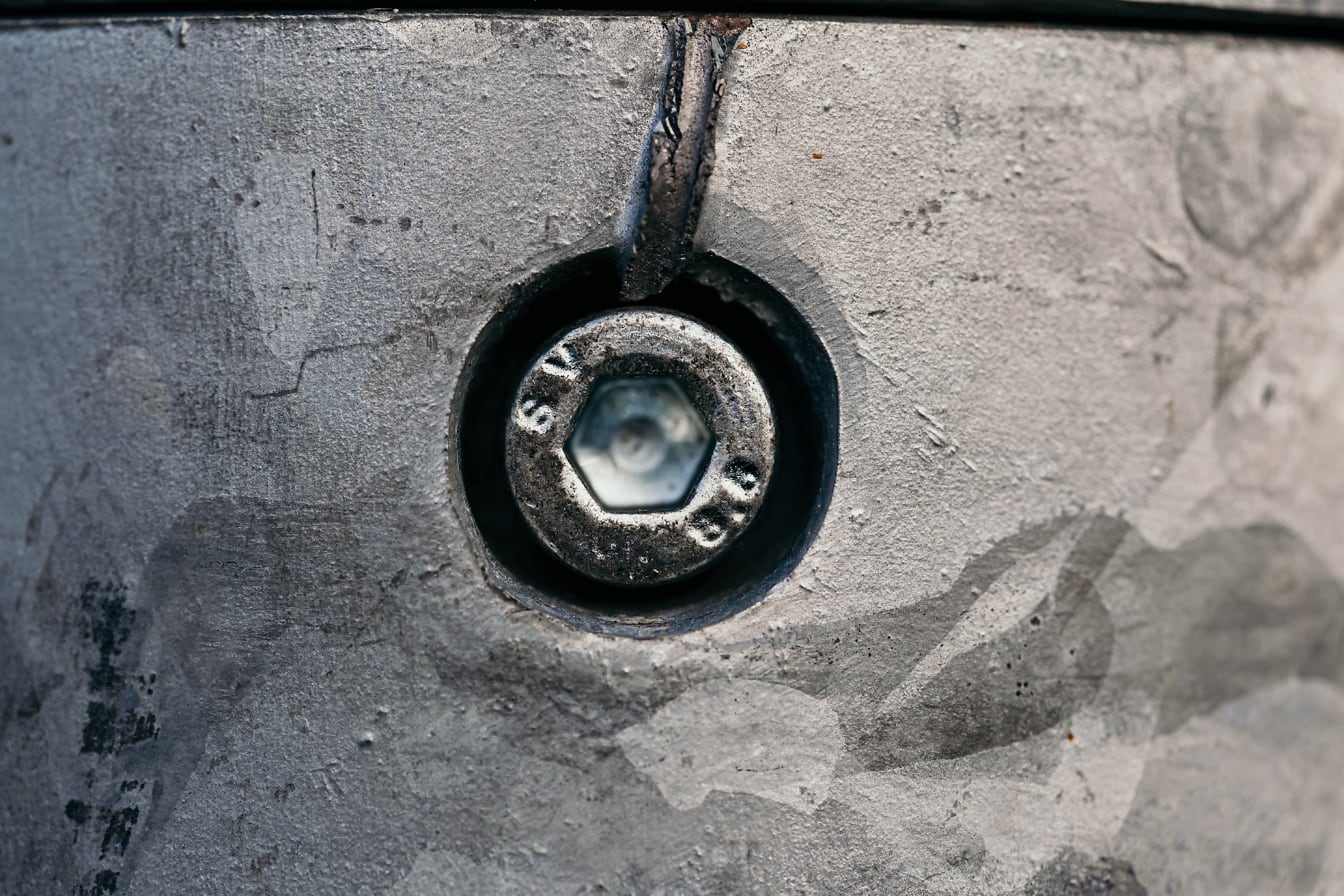 은색 금속 페인트로 칠해진 주철 표면의 구멍에 있는 강철 나사