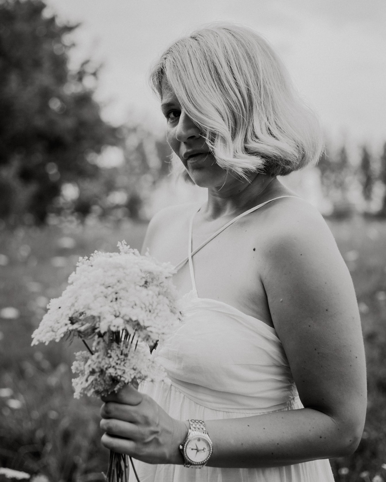 Блондинка в сватбена рокля, държаща цветя в поле, черно-бяла снимка