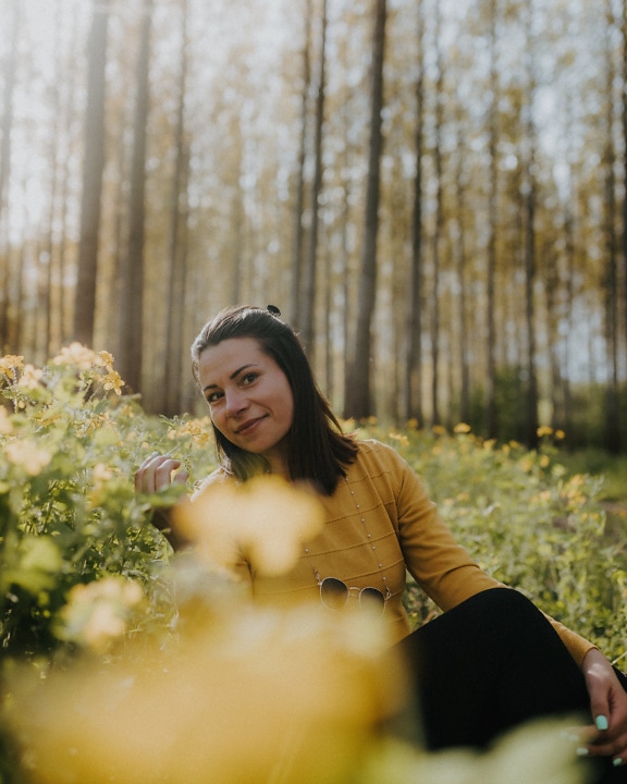 Leende brunettkvinna med det nätta ansiktet som sitter i ett fält av blommor på solig dag