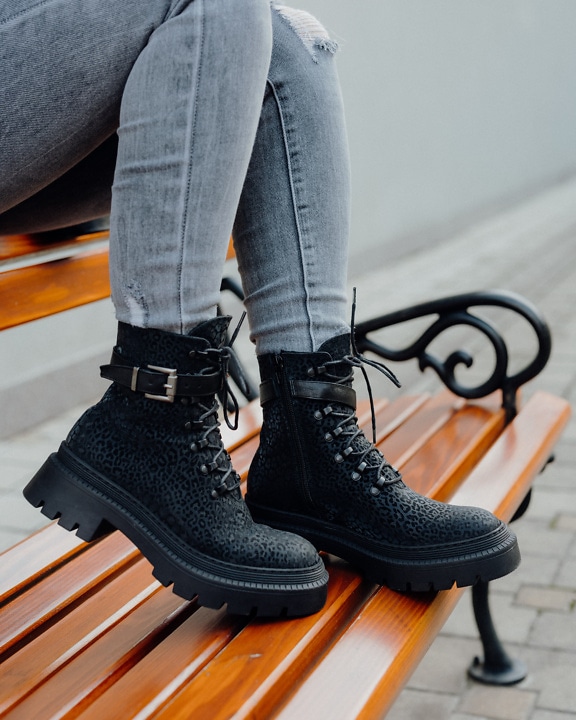 Τα πόδια του ατόμου σε σκισμένα τζιν, παντελόνια και μοντέρνες μαύρες μπότες