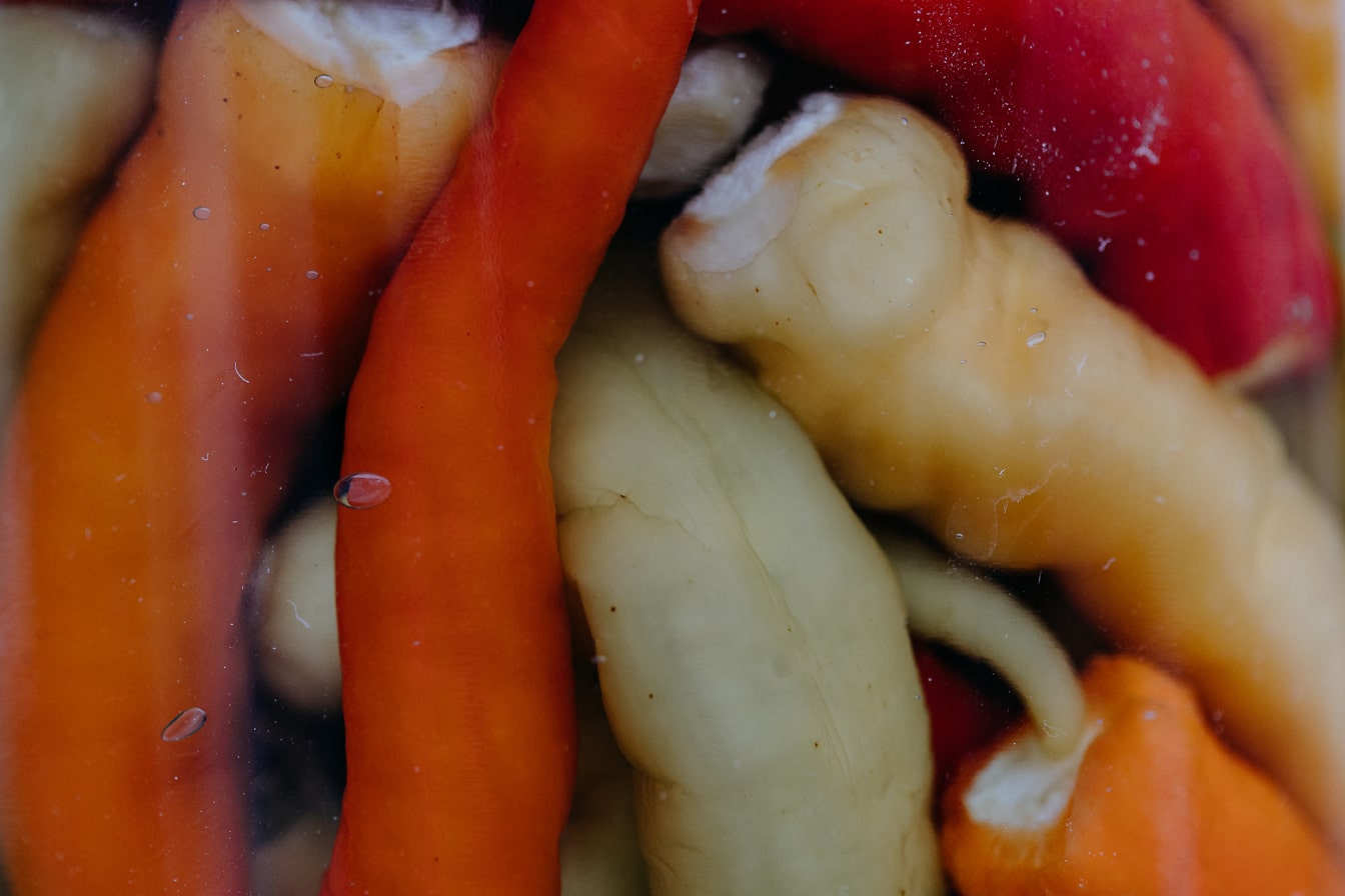 Tampilan close-up paprika kalengan oranye-kuning dalam toples