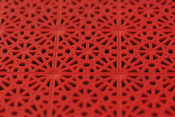 Textur av en röd plastyta med geometriskt mönster i arabeskstil