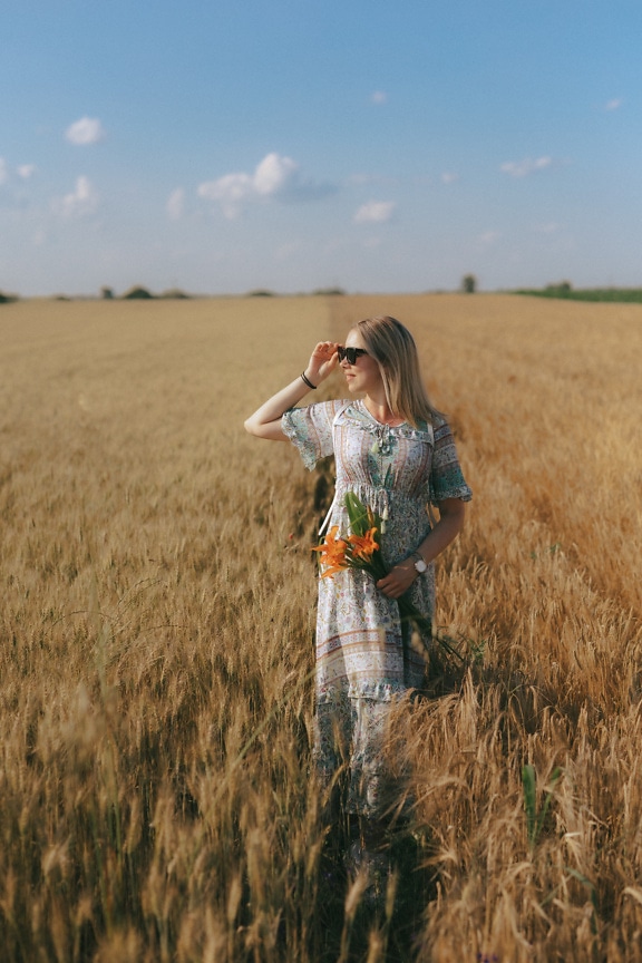 Người phụ nữ nông thôn xinh đẹp trên cánh đồng lúa mì với hoa loa kèn trên tay