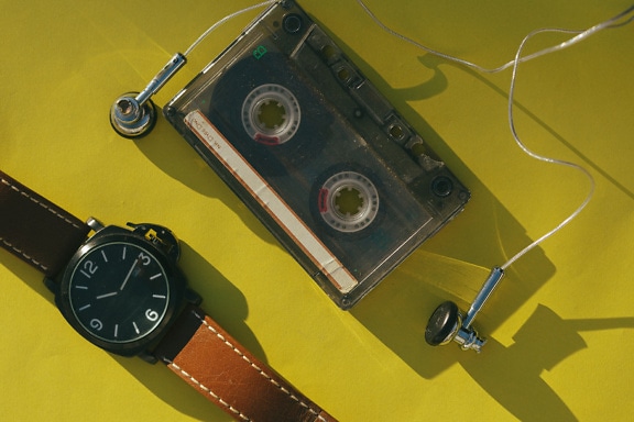 Cinta de casete de audio, auriculares y reloj de pulsera sobre una superficie amarilla