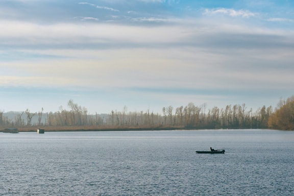 Malá rybářská loďka ve vodě s rybářem ve větrném dni