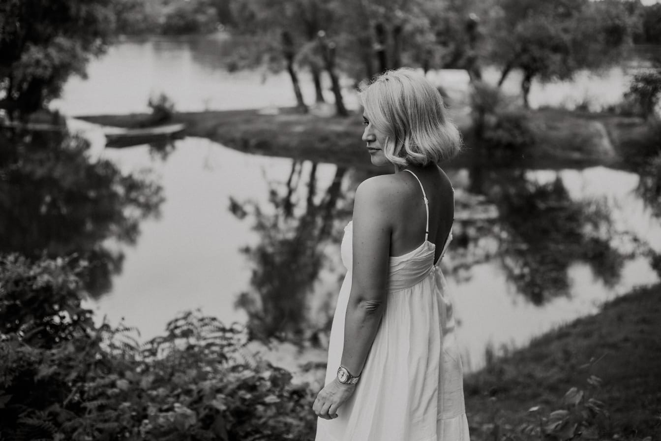 Woman in a white backless dress posing  by a lake, black and white photograph