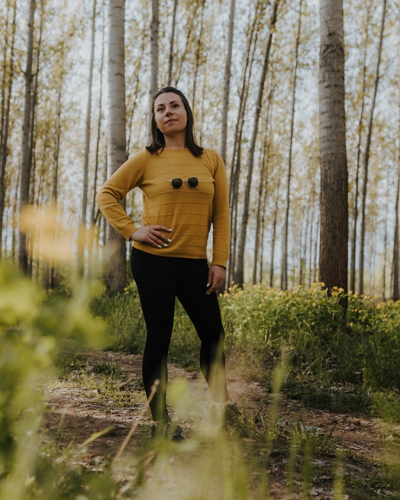 Красива жінка з гарним обличчям стоїть у лісі в жовтувато-коричневому светрі