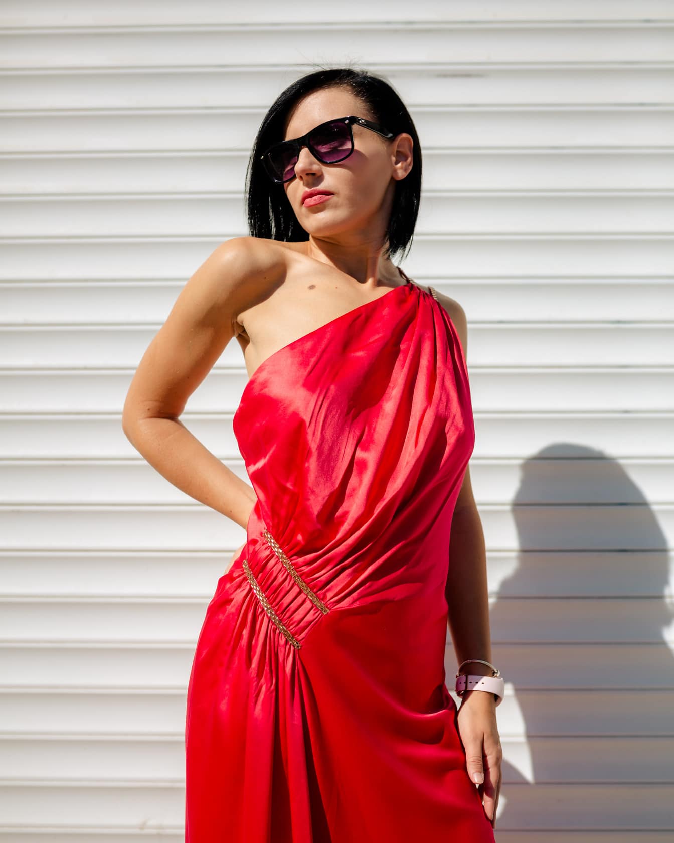 Πορτρέτο της όμορφης λεπτής γυναίκας που ποζάρει σε ένα κόκκινο μεταξένιο φόρεμα