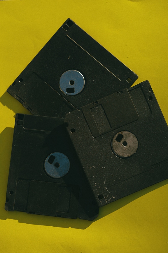 Old black floppy disks on a yellow surface