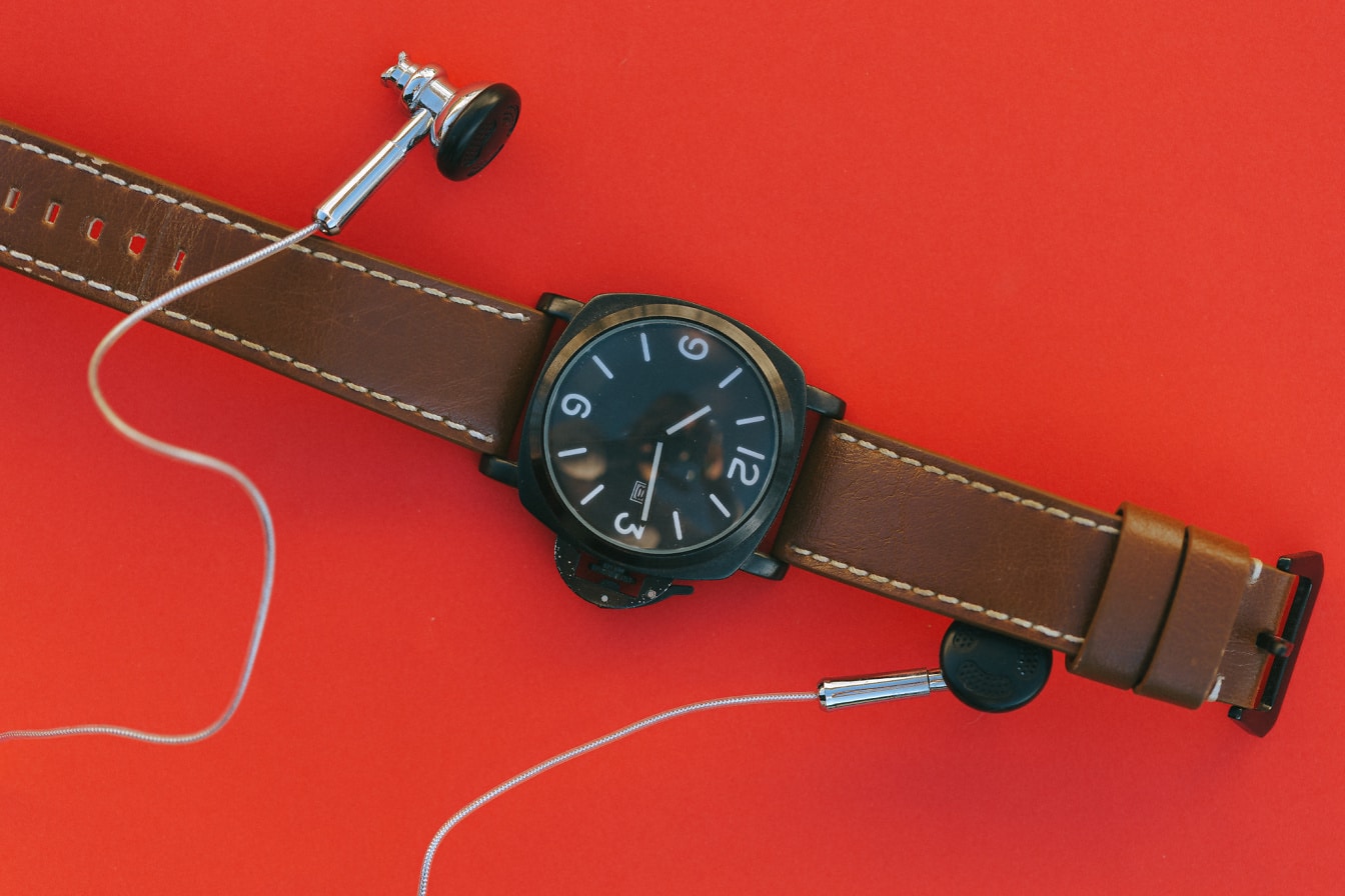 Náramkové hodinky s hnedým koženým opaskom a slúchadlami do uší
