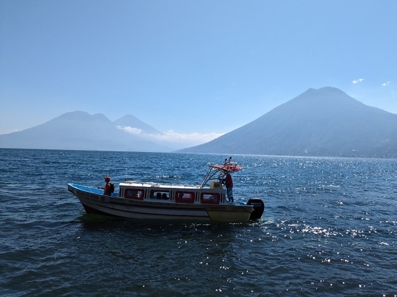 Perahu wisata kecil di danau Atitlán dengan pegunungan di latar belakang