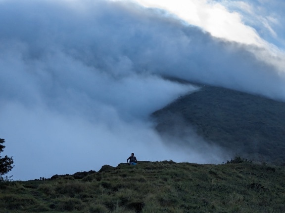 Osoba siedząca na wzgórzu z chmurami w tle