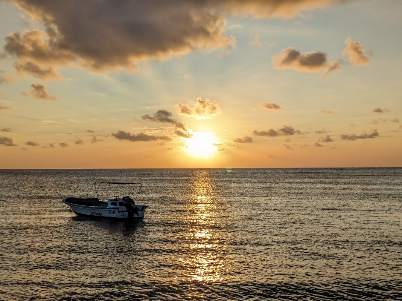 Small boat on sea with bright sunrays reflected on sea horizon at sunrise