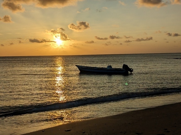 Silhuet af lille fiskerbåd på havstrand ved solnedgang