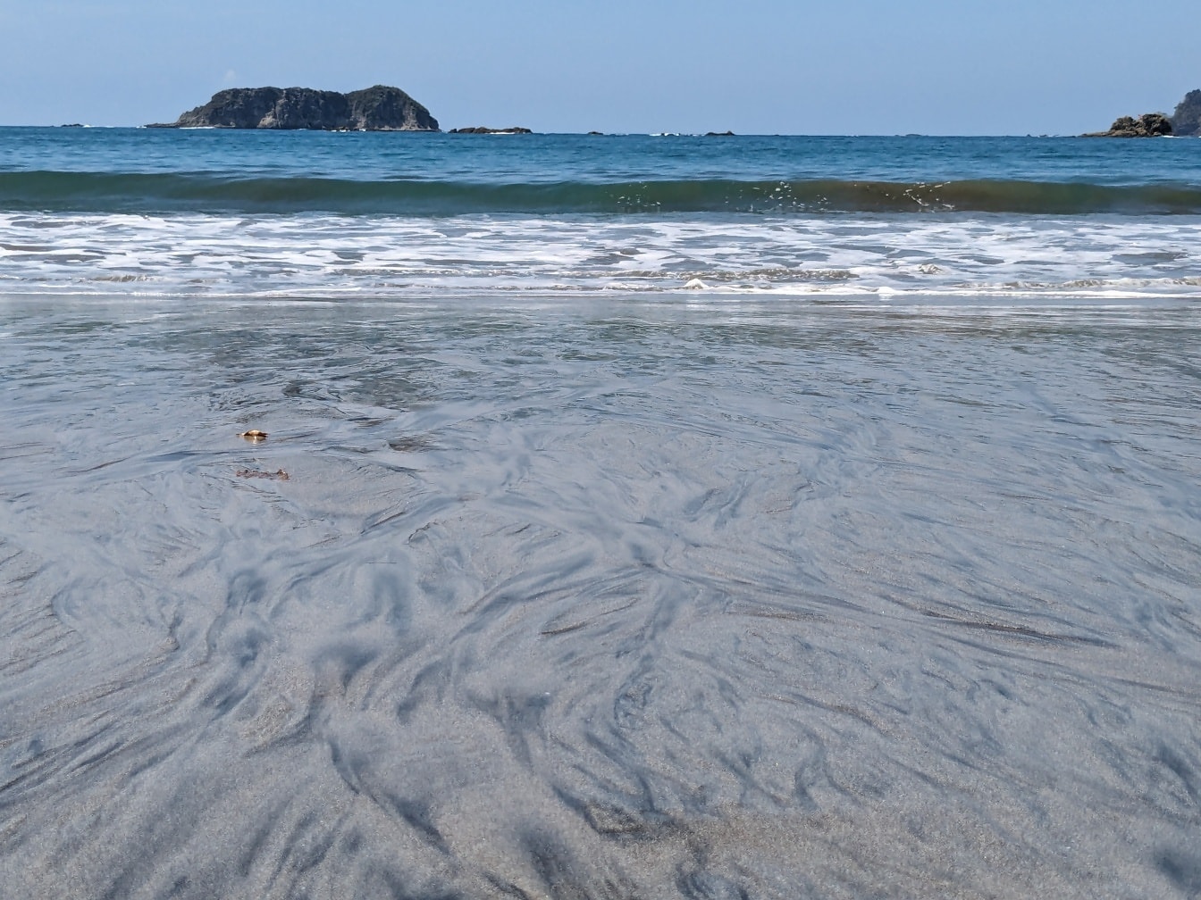 Sandstrand med bølger og lille ø i baggrunden