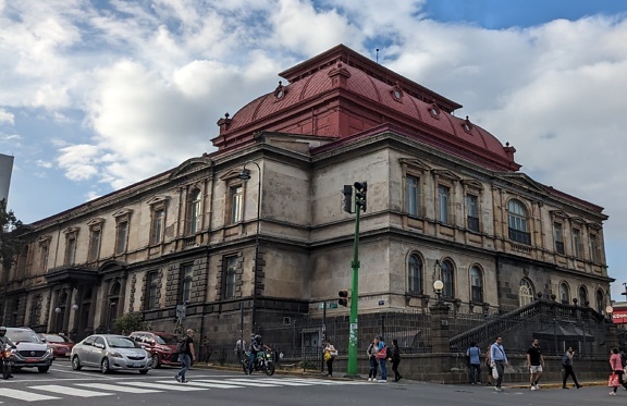 Národné divadlo Kostariky s červenou strechou a ľuďmi kráčajúcimi po ulici